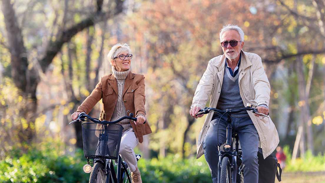 Älteres Ehepaar fährt mit Fahrrädern durch einen Park. 