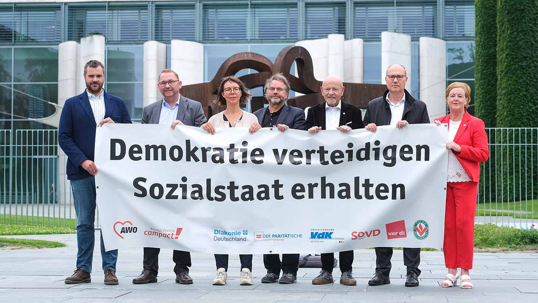 Sieben Personen halten ein Transparent mit derAufschrift "Demokratie verteidigen - Sozialstaat erhalten" vor dem Kanzleramt. 