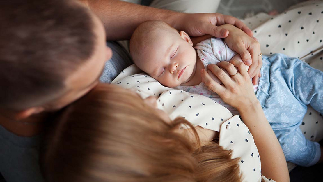 Junge Eltern halten ein schlafenden Baby.