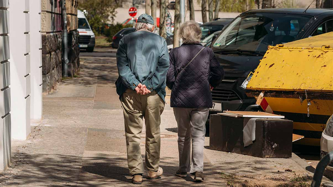 Rentnerpärchen läuft eine Straße hinab. 