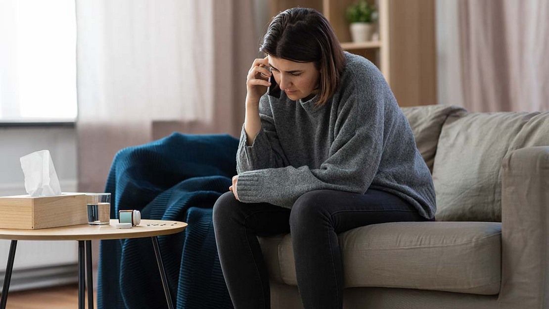 Niedergeschlagene Frau sitzt auf einer Couch und telefoniert. 