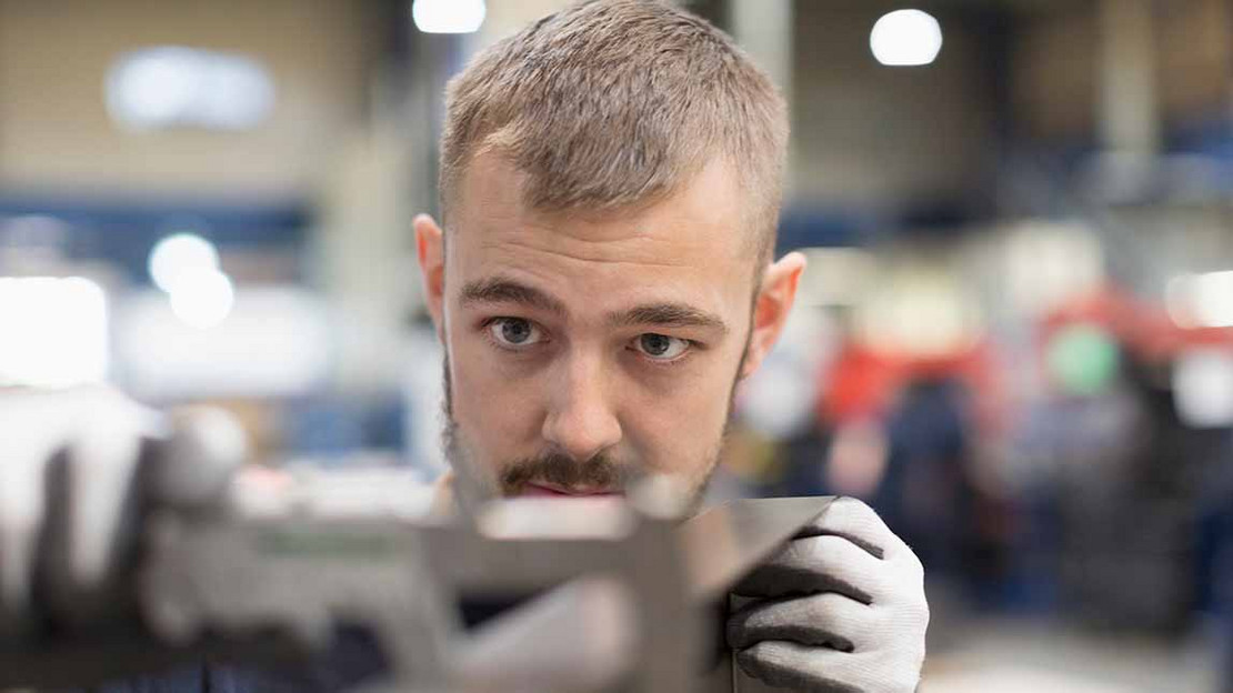 Mann in einer Fabrik arbeitet konzentriert an einer Maschine. 