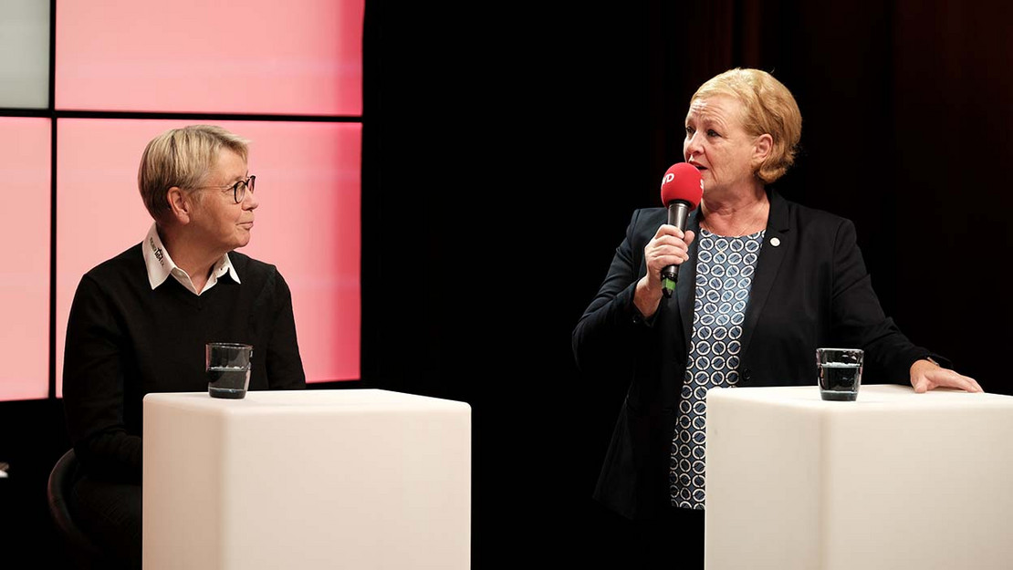 Zwei Frauen im Studio, eine hält ein Mikrofon. 