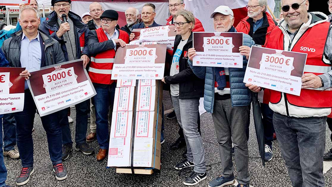 Gruppe von Menschen mit Schildern und der Schrift "3000 Euro auch für Rentner*innen". 
