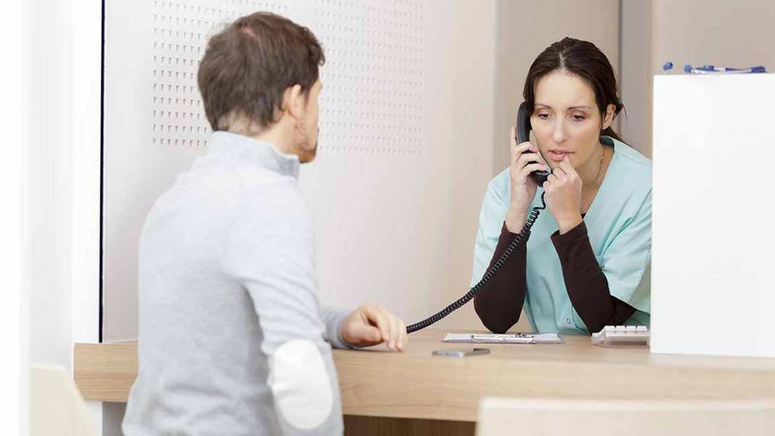 Mann am Empfang eines Krankenhauses. Frau redet am Telefon. 