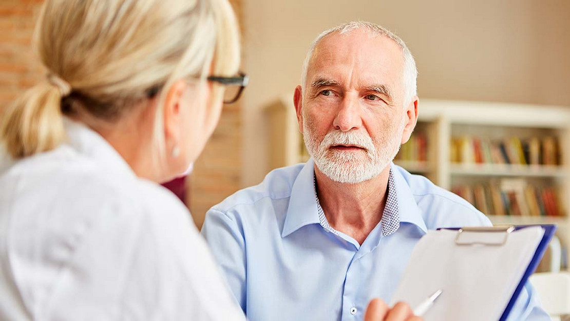 Ein älterer Patient sitzt einer Ärztin gegenüber, die ihm etwas erklärt.