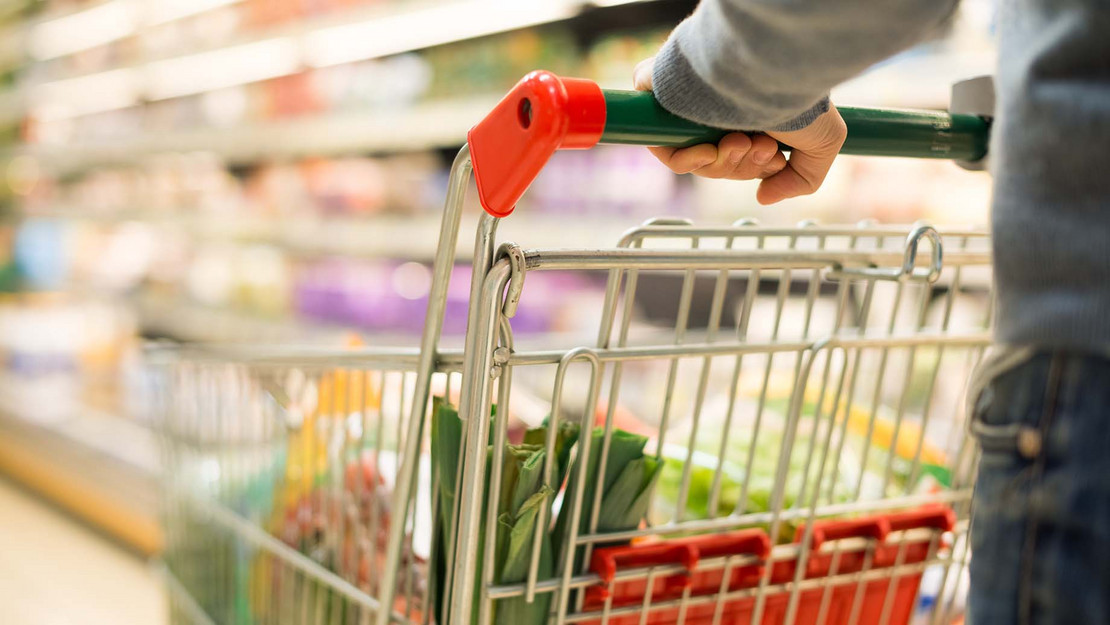 Mensch schiebt Einkaufswagen durch einen Supermarkt