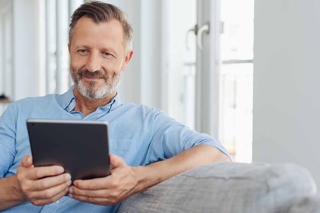 Mann sitzt auf der Couch und liest auf seinem Tablet. 