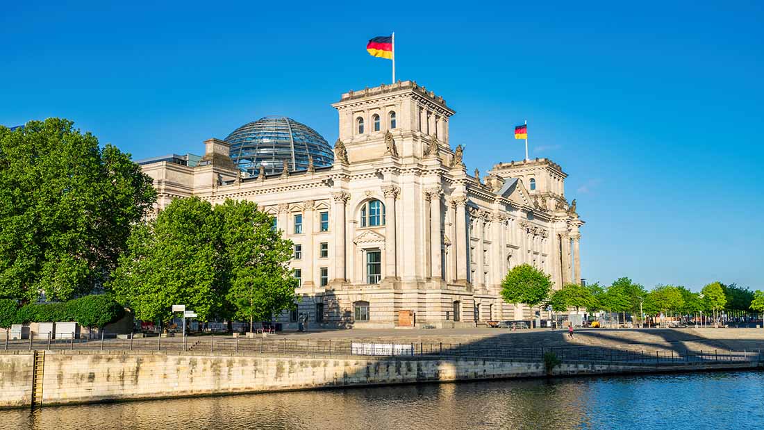 Reichstagsgebäude in Berlin bei Sonnenschein von der gegenüberliegenden Spreeseite aus fotografiert.